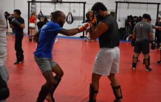 Mixed martial artists sparring in Gilbert gym, comparing MMA and BJJ strategies in training.