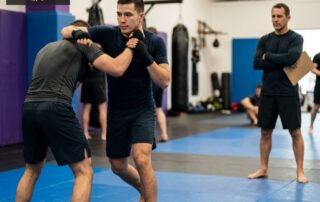 Adult MMA athlete transitioning from a standing strike into a clinch position with a coach observing at Arizona Combat Sports in the East Valley, Arizona