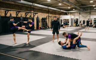 Wide gym view of an integrated MMA class at Arizona Combat Sports showing striking drills and ground grappling on the same mat, Arizona